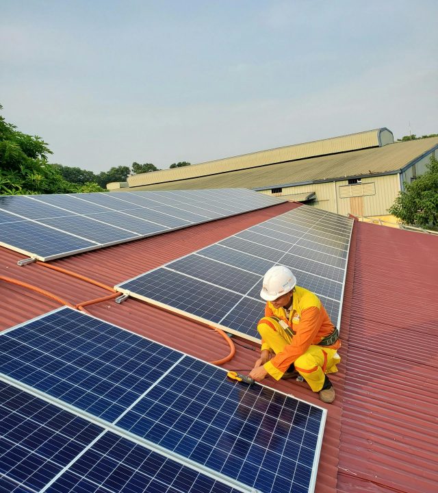Technician working on solar panel installation on a rooftop under clear sky.